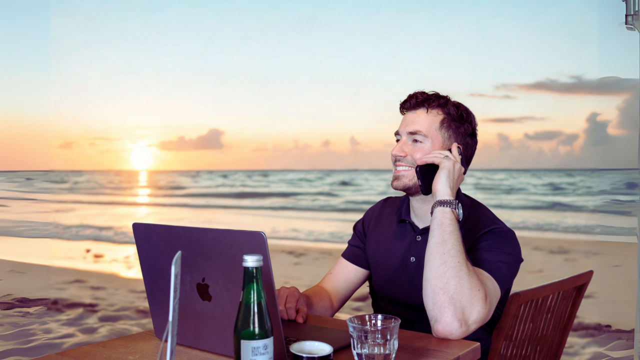 Beau werkend op het strand aan een bureau met laptop